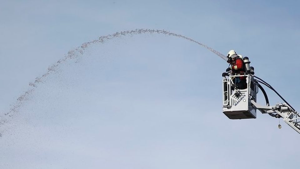Feuerwehrmann auf einer Hebebühne spritzt mit Wasser.