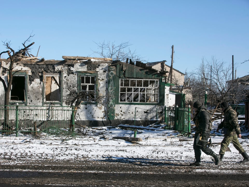 Pro-russische Separatisten laufen an einem zerstörten Haus vorbei