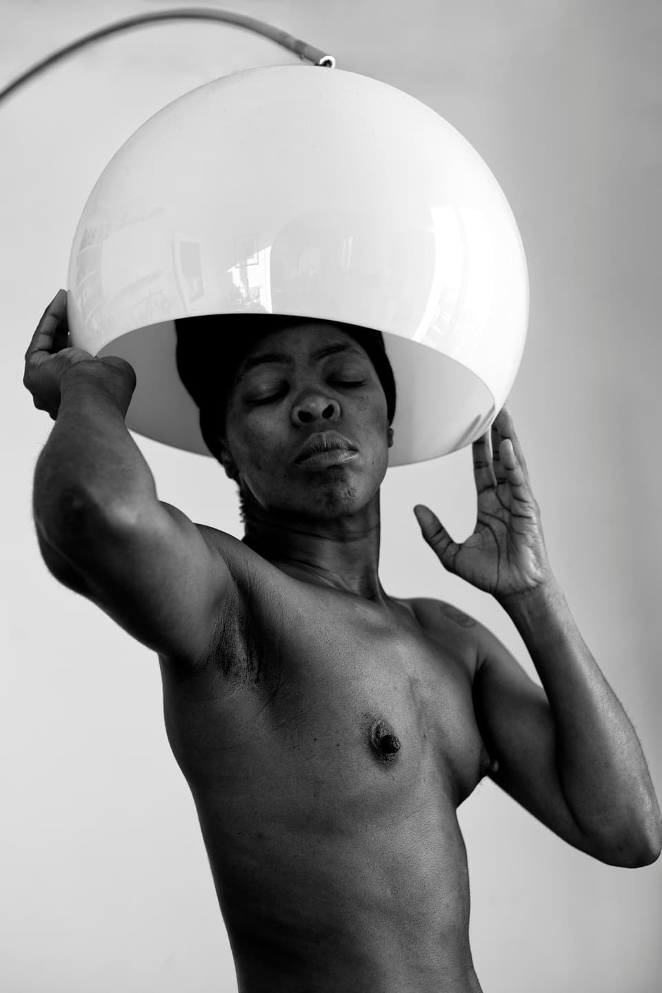 Schwarz-Weiss-Porträt einer oberkörperfreien schwarzen Person unter einem Lampenschirm