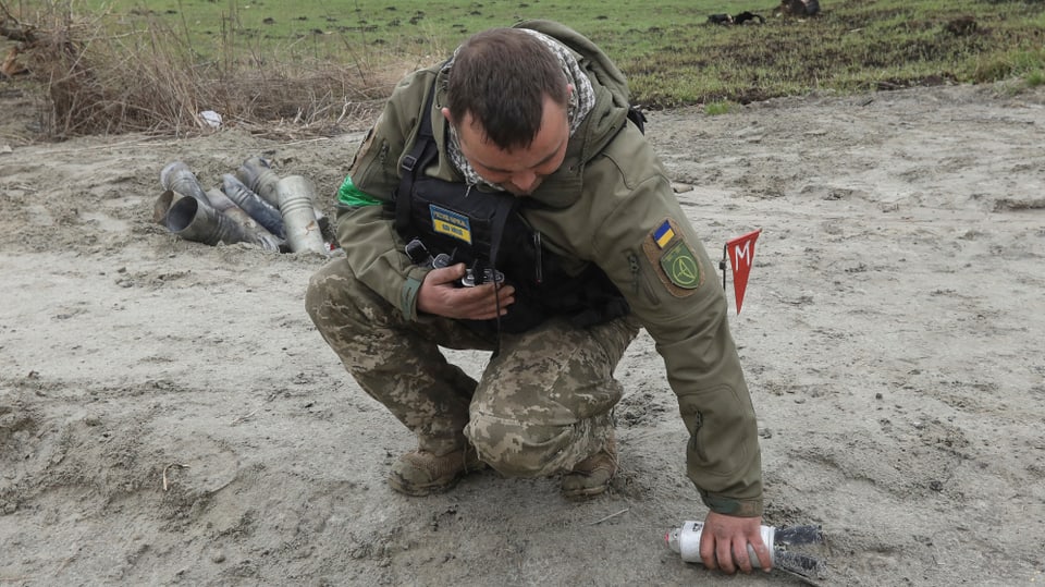 Ukrainischer Soldat hebt nach dem russischen Einmarsch die Hülse einer Streubombe auf.