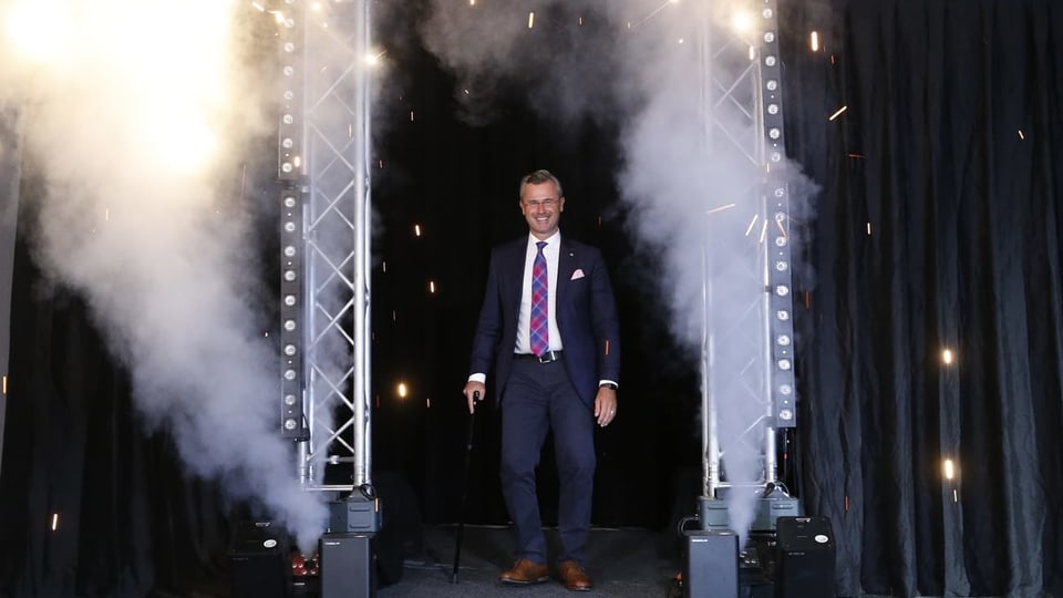 Der Wahlgewinner Norbert Hofer schreitet durch einen mit Feuerwerkskörpern geschmückten Rahmen.