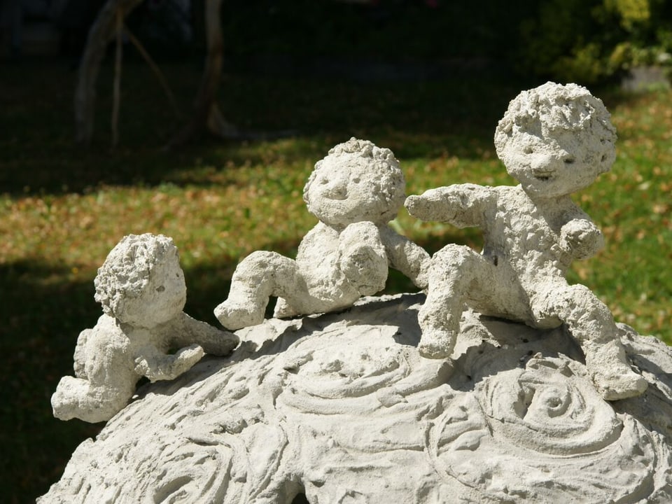 Nahaufnahme einer kugelförmigen Skulptur auf der drei spielende Kinder aus Lehm sitzen.