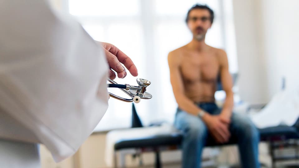 Behandlung beim Hausarzt: Ein Mann sitzt auf einer Untersuchungsliege. 