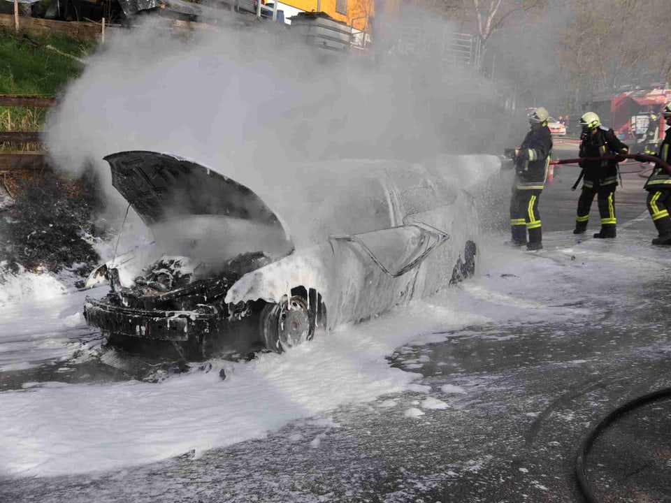 Ausgebranntes Auto und Feuerwehrleute.