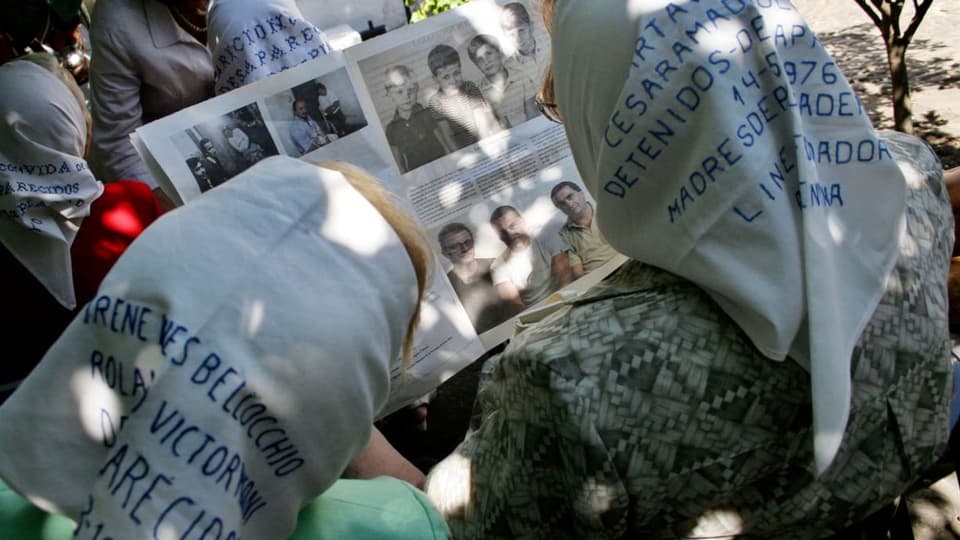 Mujeres con velos blancos escritos desde atrás miran fotografías