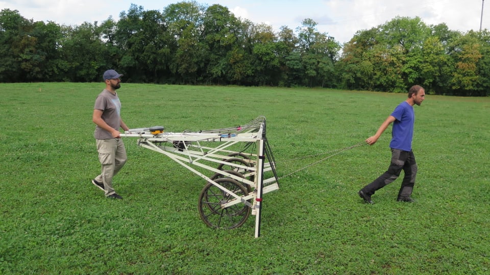 Zwei Männer ziehen ein grosses Gerät über ein Feld