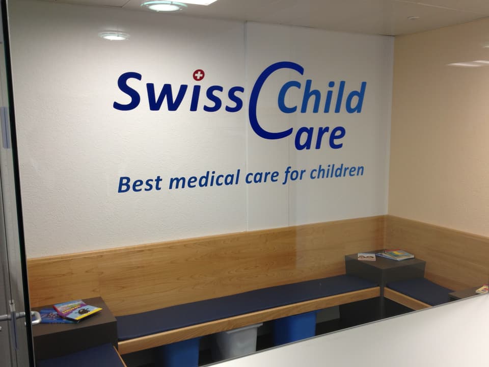 Leeres Wartezimmer im SwissChildCare Zentrums mit dem Logo des Zentrums auf der Glaswand