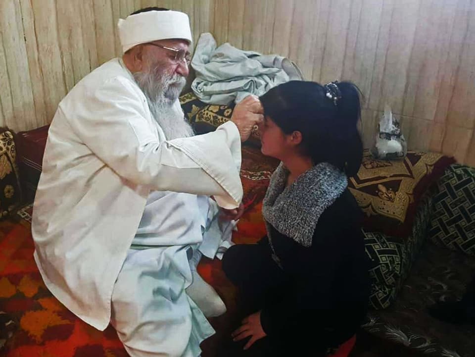 Baba Sheikh macht einer jungen Frau ein Kreuzzeichen auf die Stirne.