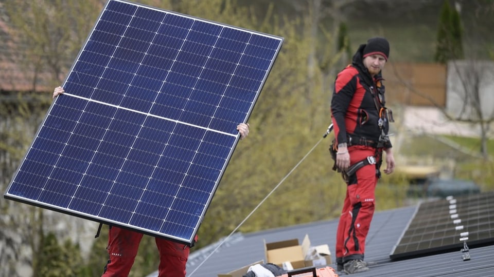 Zwei Arbeiter montieren eine Solaranlage auf einem Dach