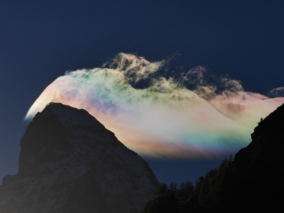 Eine Wolke hinter einem Berg mit perlmut Farben.