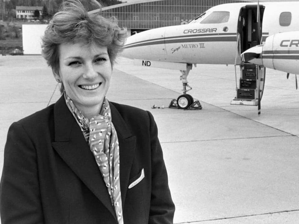 Schwarzweiss Bild, auf dem eine junge Frau in Uniform vor einem Flugzeug steht und in die Kamera lacht.