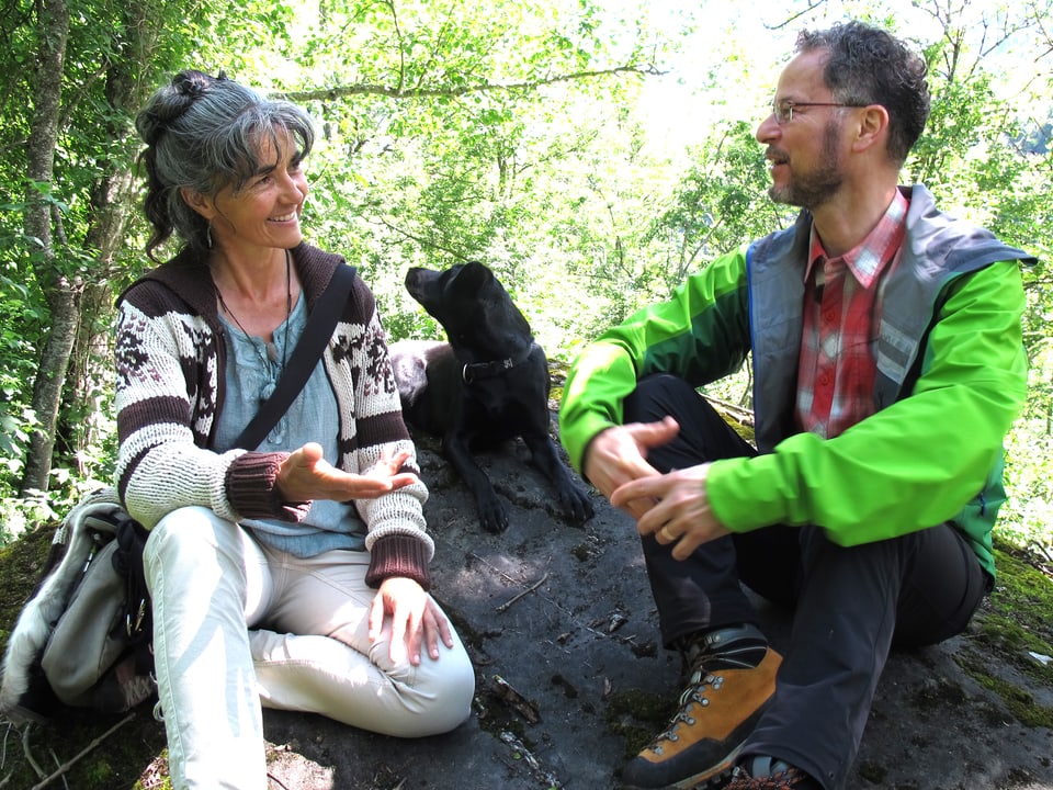 Eine Frau und ein Mann sitzen diskutierend auf einem Stein im Wald