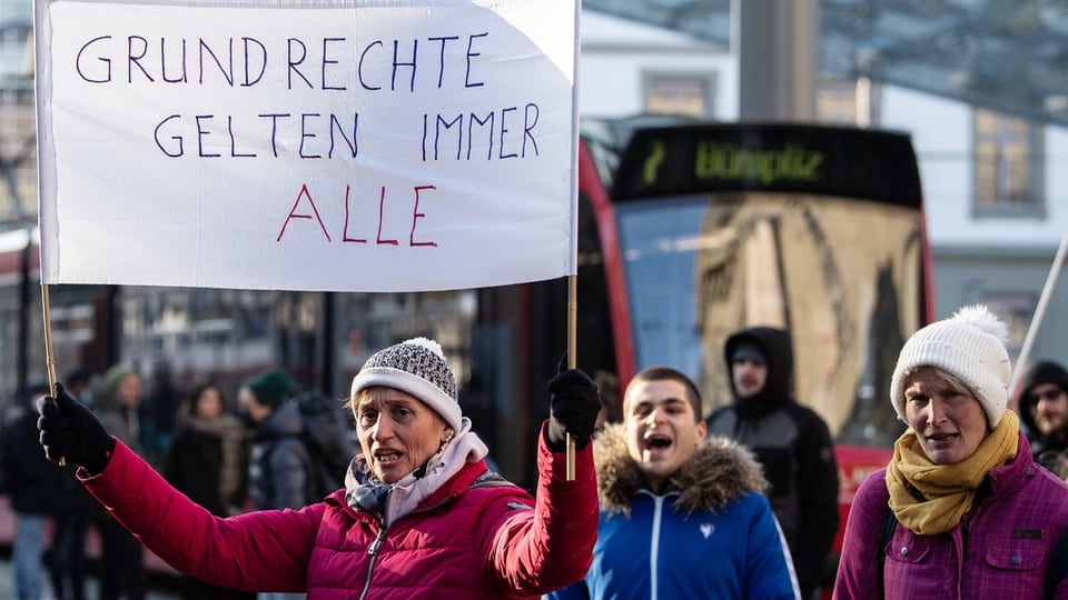 Eine Frau mit einem Schild, auf dem steht: Grundrechte gelten immer alle.