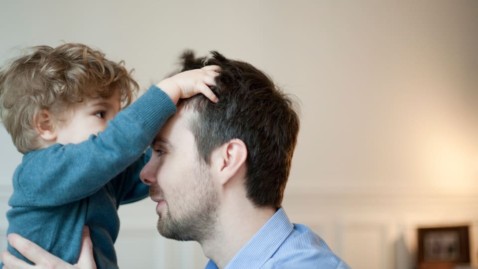 Ein Kind greift seinem Vater mit den Händen in die Haare.