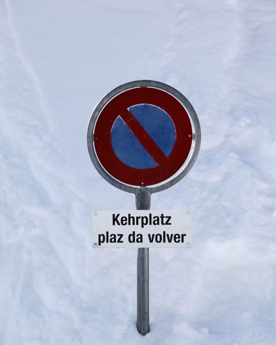 Eine Parkverbotstafel im Schnee: Darunter steht ein Informationsschild: «Kehrplatz, Plaz da volver» (rätr.)