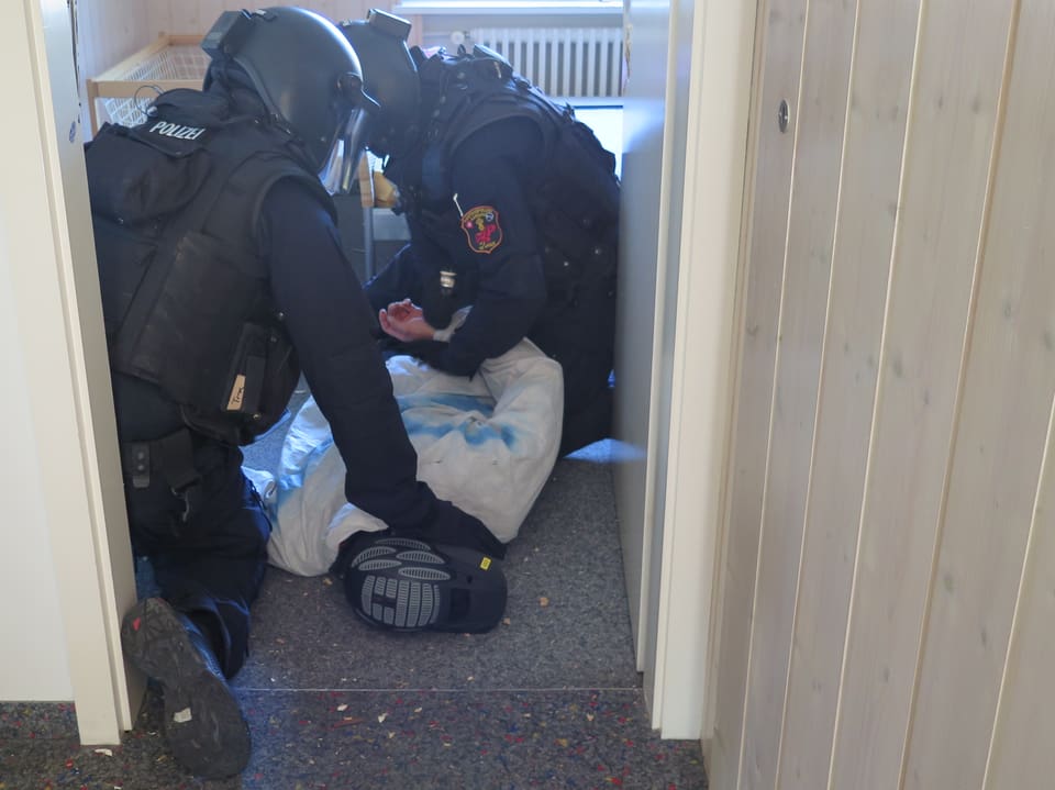 Ein Mann liegt auf dem Boden und wird von zwei Polizisten festgehalten. 