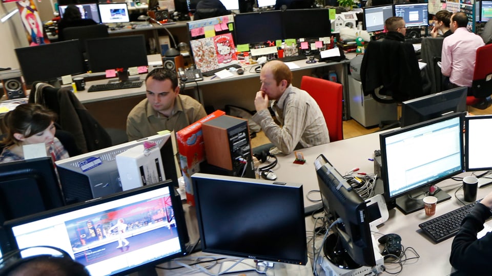 Mitarbeiter eines Unternehmens für Computerspiele sitzen zusammen vor grossen Bildschirmen.