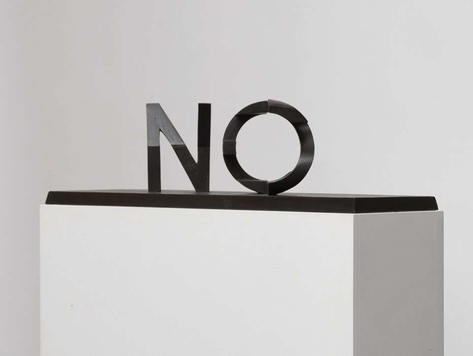 Schwarze Schriftskulptur «No» auf einem weissen Sockel, weisser Hintergrund