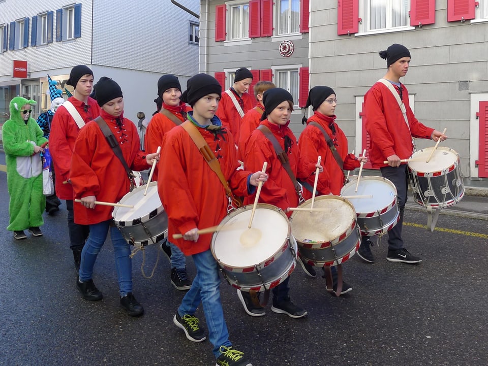 Eine Gruppe junger Tambouren zieht in roten Gewändern durchs Dorf. 