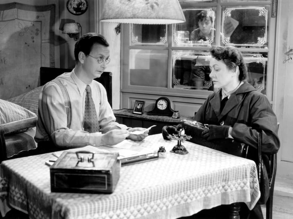 Ein Mann und eine Frau sitzen an einem Tisch und diskutieren über Papieren, die auf dem Tisch und in ihren Händen liegen.