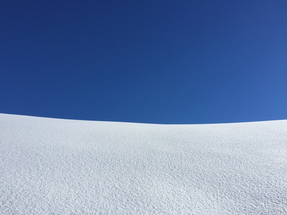 In der oberen Bildhälfte ist tiefblauer Himmel zu sehen. Unten ein unberührtes Schneefeld.