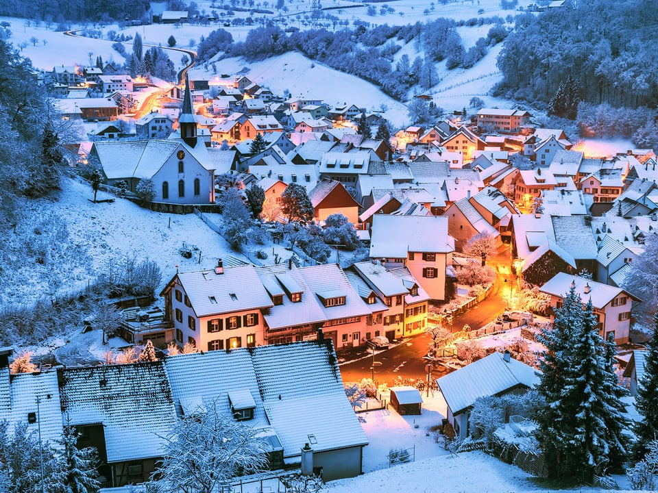 Dorf in der Dämmerung mit Lichtern und etwas Neuschnee, wie an Weihnachten.