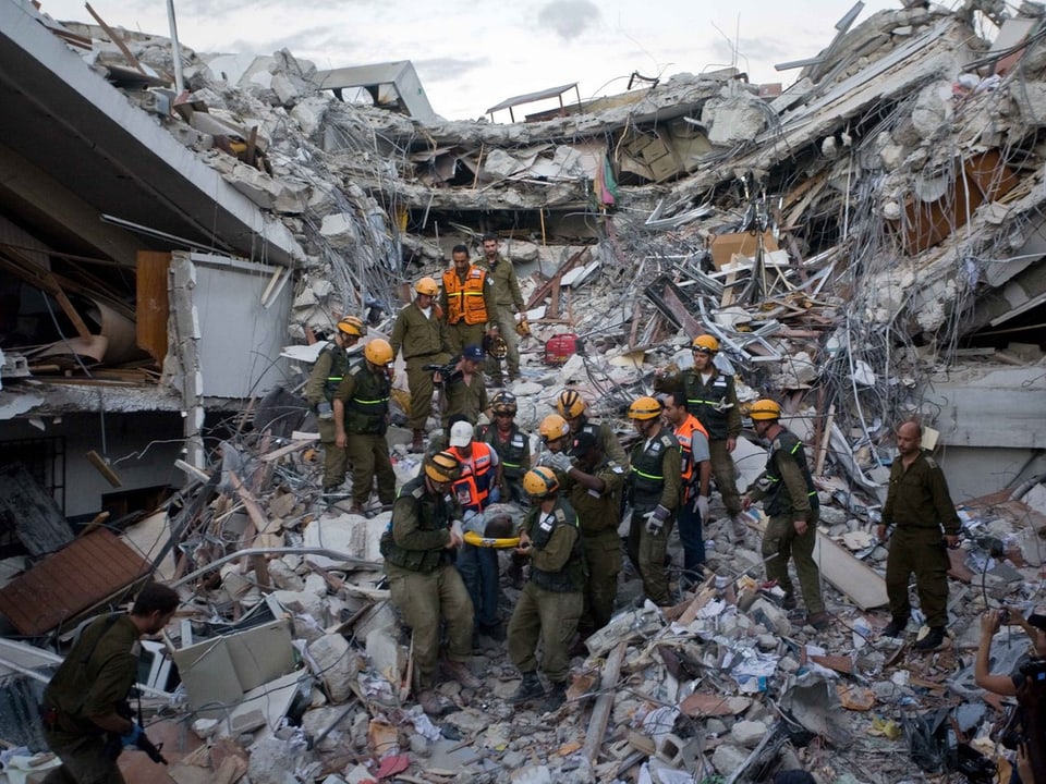 Retter tragen eine überlebende Person aus den Trümmern eines Hauses.