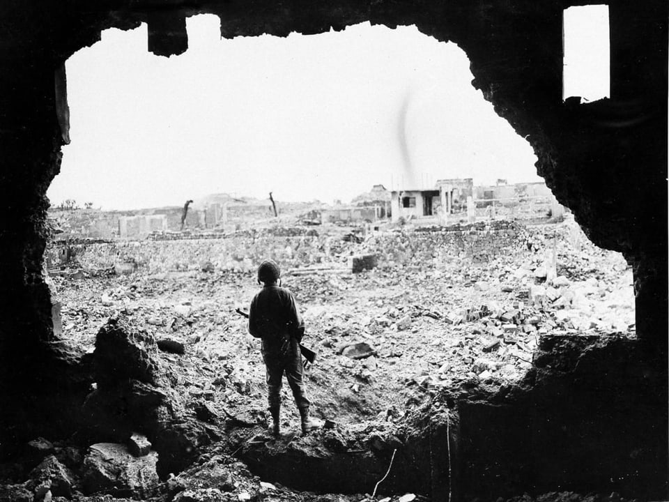 Ein Soldat blickt aus einer Ruine auf die zerstörte Stadt.