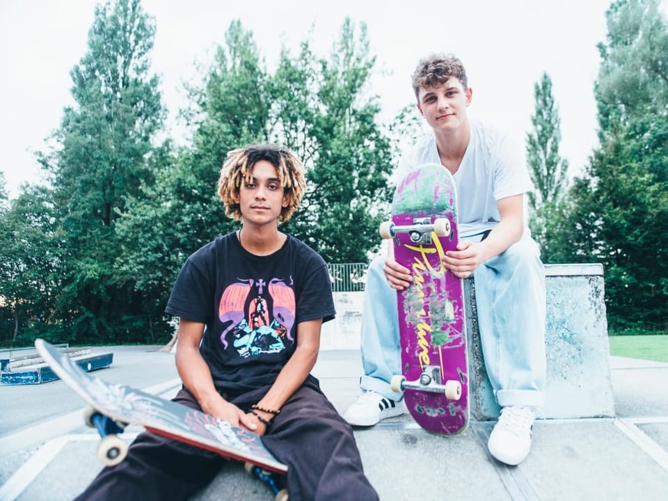 Zwei junge Menschen sitzen auf einer Rampe im Skatepark.