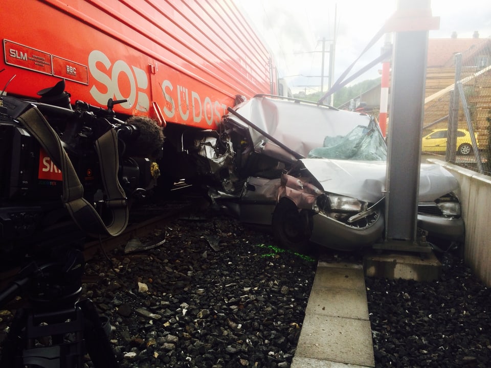 Ein zertrümmertes und zerdrücktes Auto neben einem roten Zug. 