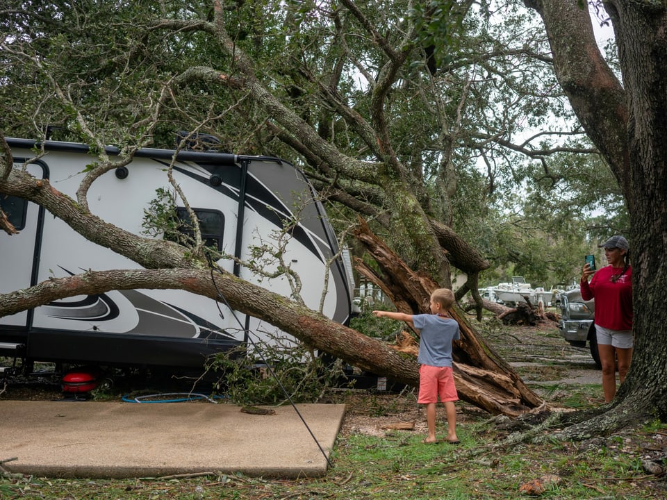 Zwei Personen inspizieren einen Camper-Wagen, der wegen dem Sturm von einem Baum getroffen wurde.