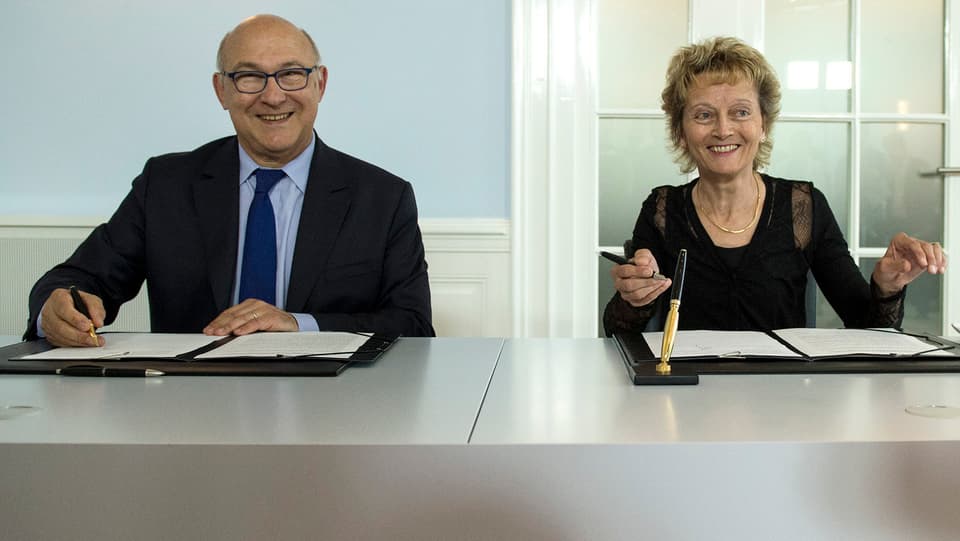 Finanzminister Michel Sapin und Bundesrätin Eveline Widmer-Schlumpf lachen bei der Vertragsunterzeichnung.
