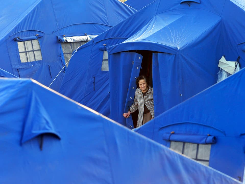 Alte Frau schaut aus einem blauem Zelt, die für die obdachlosen Erdbeben-Opfer errichtet wurden.