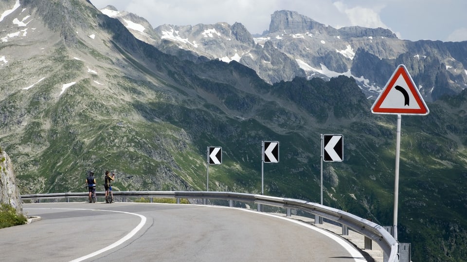 zwei Velofahrer fotografieren von einer Kurve aus die Berge