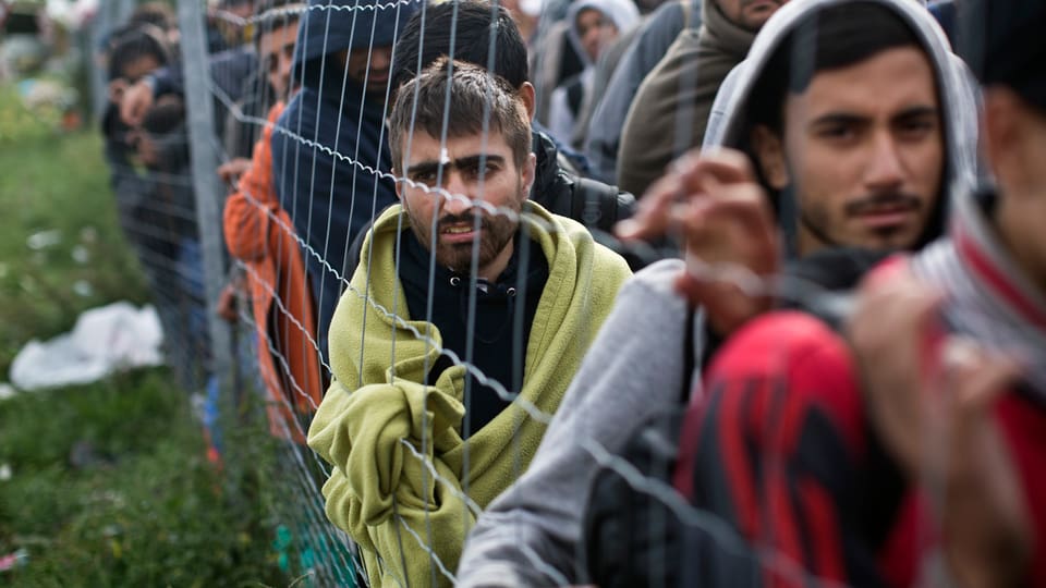 Flüchtlinge an einem Grenzzaun.