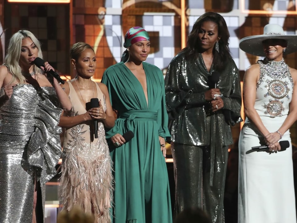 Fünf Frauen stehen in Kleidern auf einer Bühne mit Mikrofonen.
