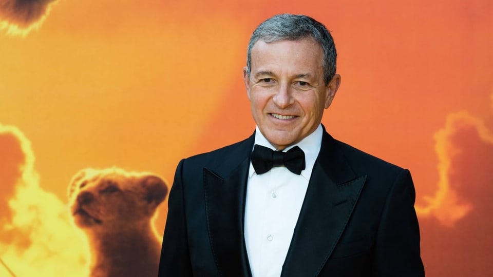 man in black tuxedo standing in front of poster with orange sky and baby lion. 