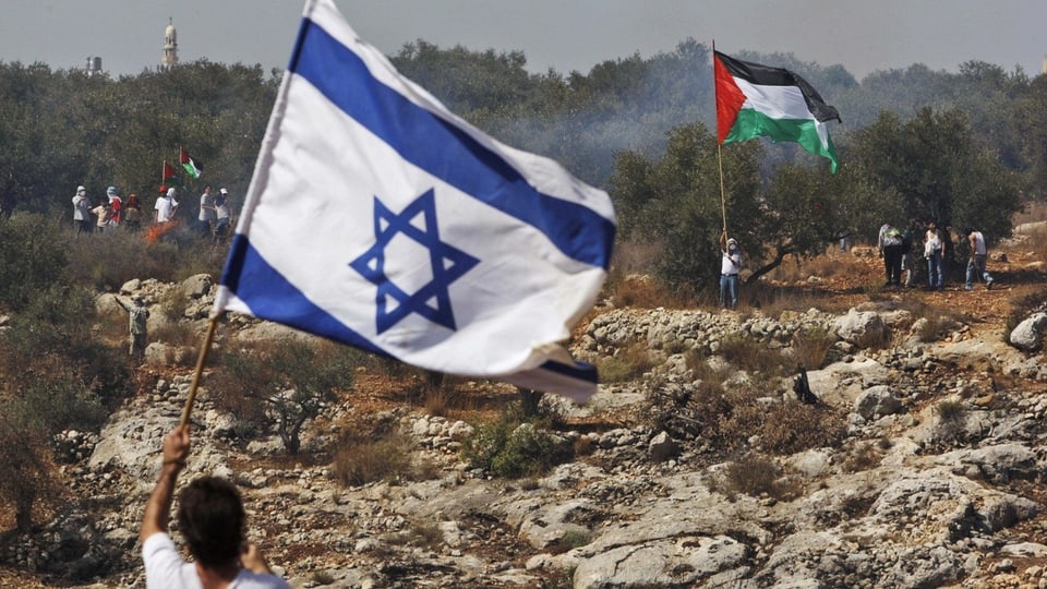 Zwei Männer stehen weit weg voneinander. Einer von ihnen hält eine israelische Flagge und einer eine palästinensische.