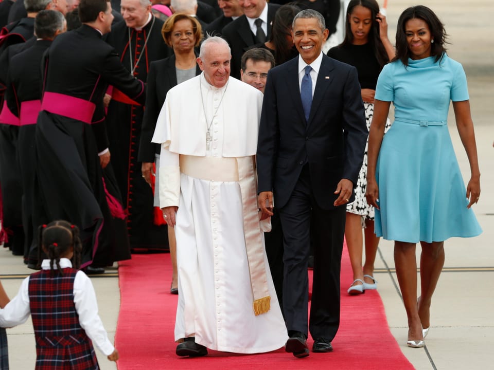 Barack Obama und der Papst schreiten über einen roten Teppich.