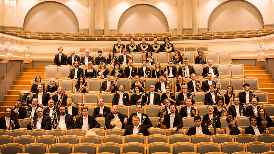 Mitglieder des Orchesters sitzen in den Zuschauerrängen.