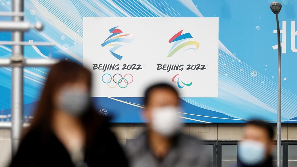 Fussgänger laufen in Peking an einer Werbung für die Olympischen Winterspiele vorbei.