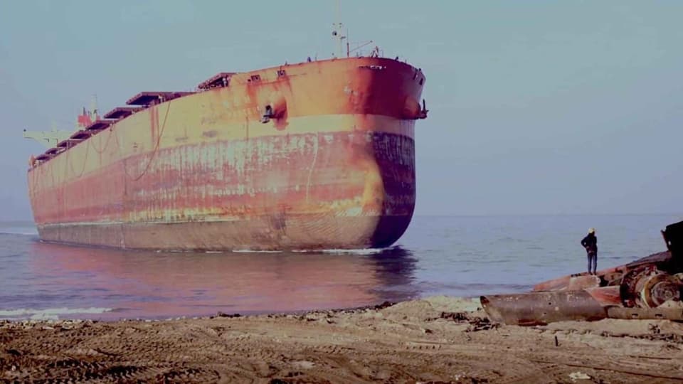 Rostiges Frachtschiff vor einer Küste.