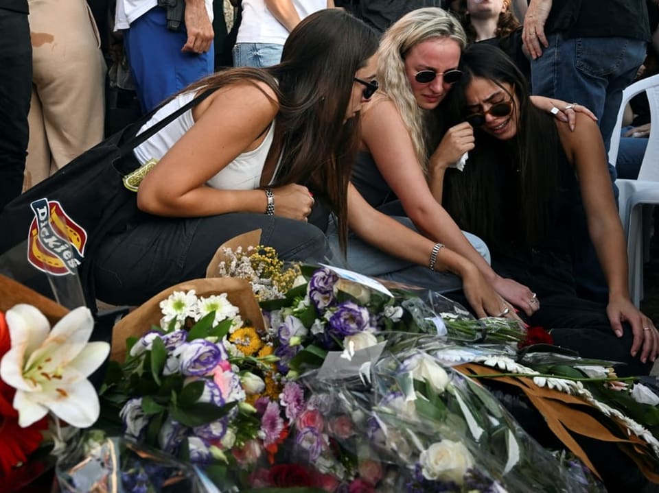 Frauen trauern um Grab mit Blumen