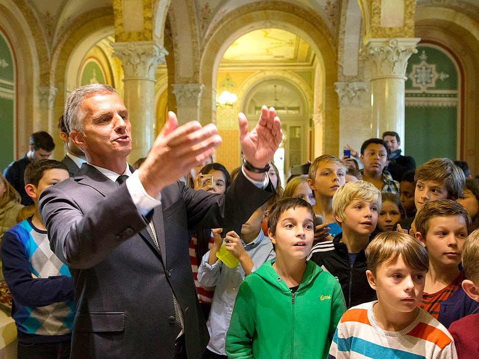 Didier Burkhalter zeigt mit den Händen in den Raum, die Blicke der Kinder folgen ihm.