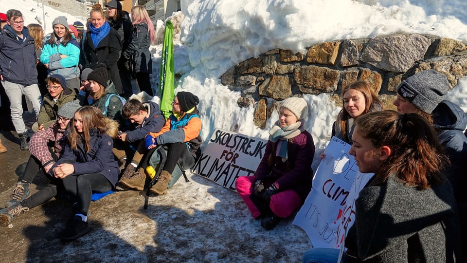 Schülerinnen und Schüler sitzen in Davos neben Greta Thunberg am Boden.