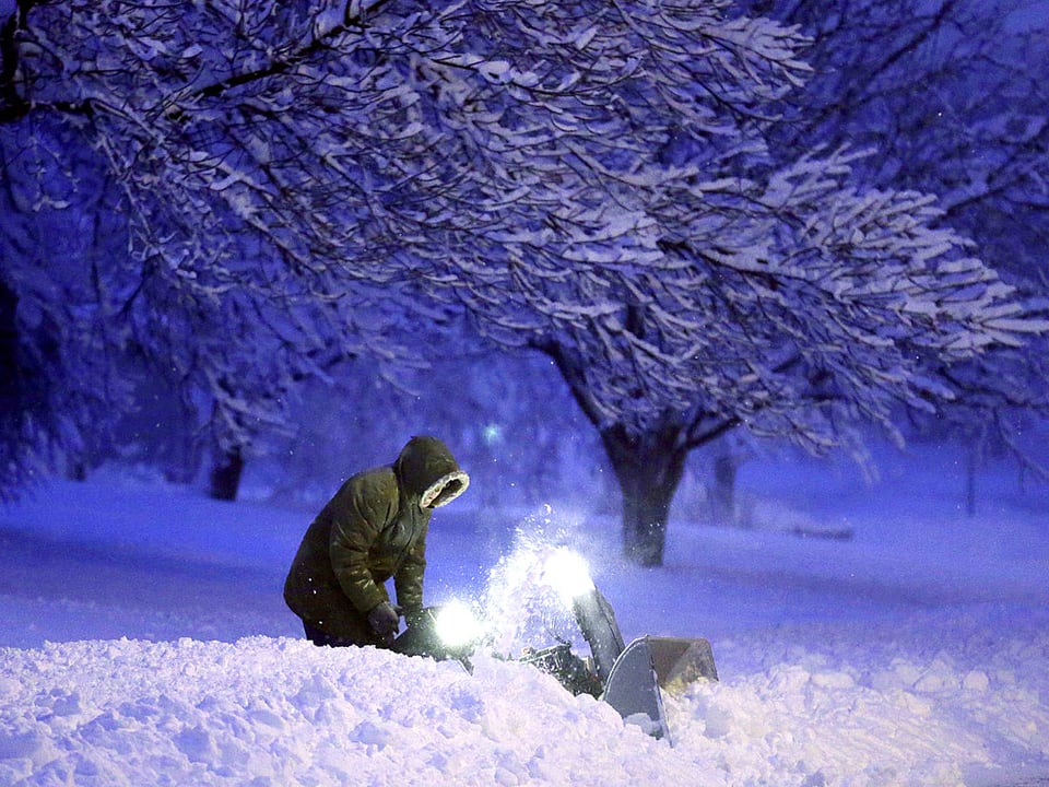 Ein Mann kämpft gegen die Schneemassen mit einer kleinen Schneefräse. Die Szenerie ist in blaues Licht getaucht.