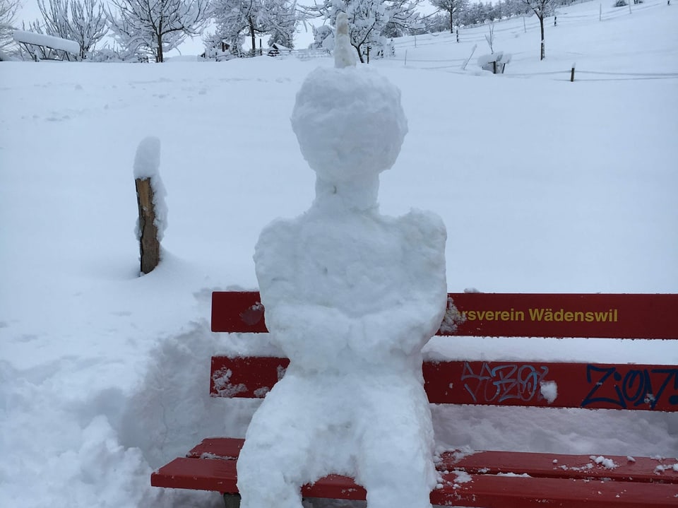Ein Schneemann hat es sich auf der Parkbank gemütlich gemacht.