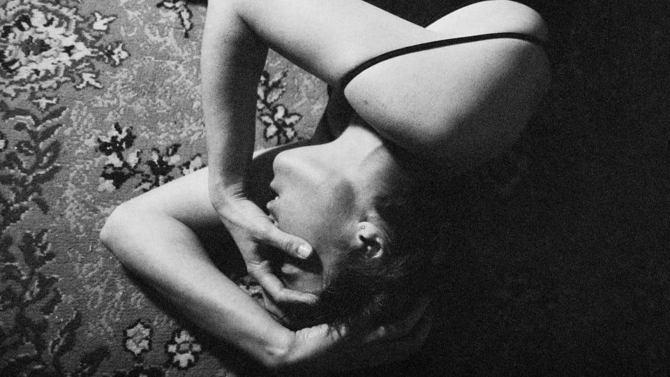Schwarz-Weiss-Bild einer jungen Frau, die am Boden liegt und die Hände vors Gesicht hält.