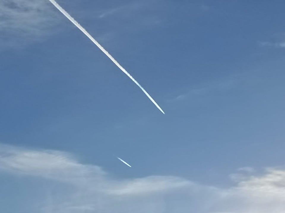 Kondensstreifen. Einmal ein langer gut ausgebildeter und einmal ein kleiner. Vor blauem Himmel mit dünnen Wolken.