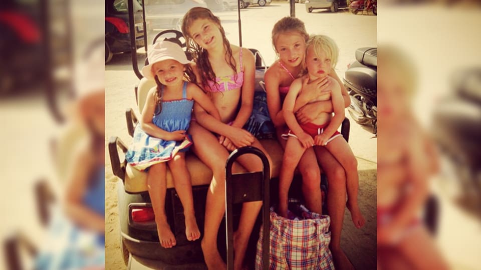 Vier Kinder sitzen in Sommeroutfits da und lächeln.